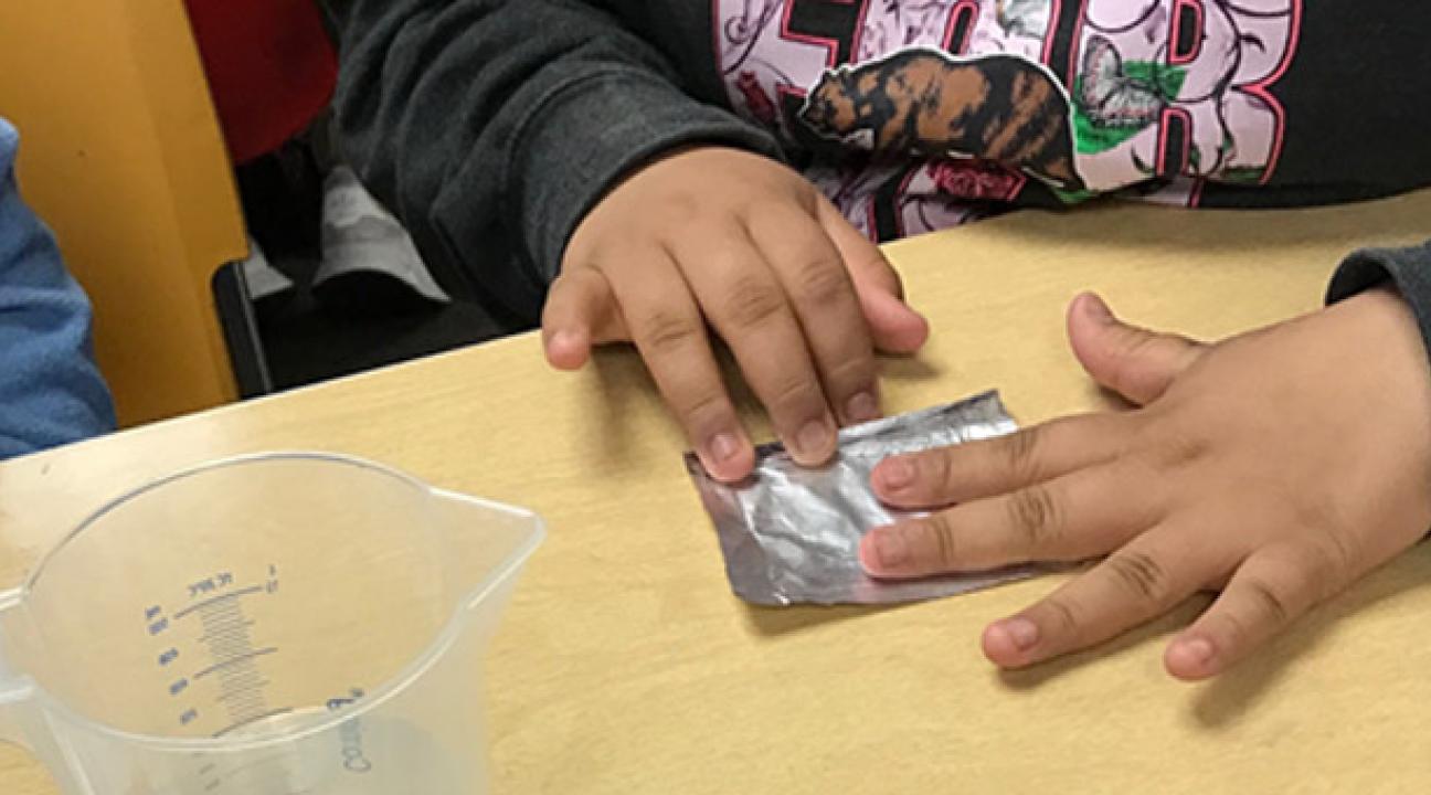 Student flattening a small piece of foil on a table.