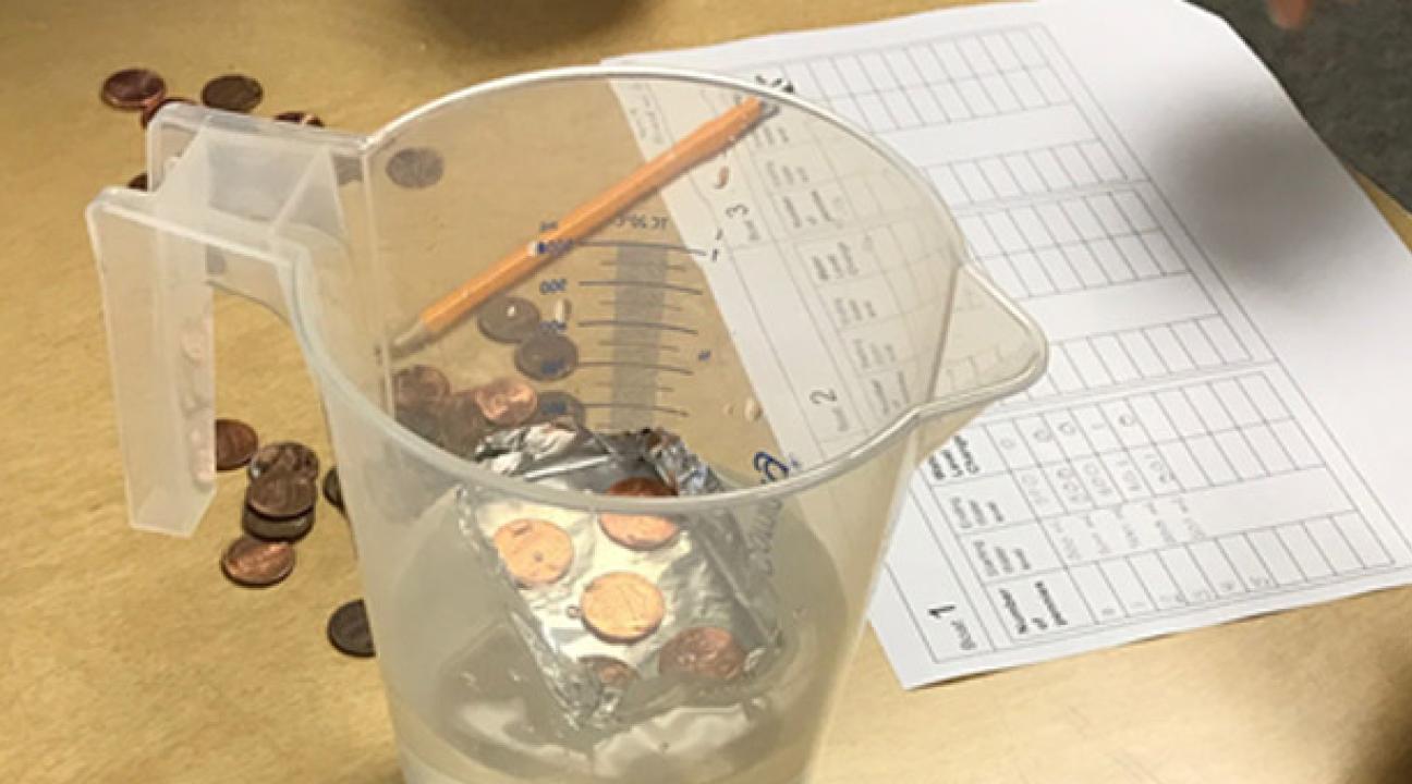 Coins and spreadsheet on a table next to a pitcher of water.