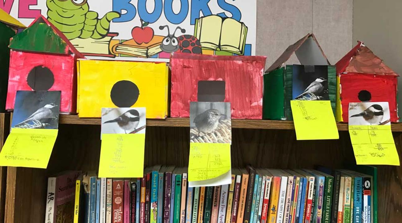 5 birdhouses on top of a bookshelf.  There are 3 red, 1 yellow and 1 green birdhouses.