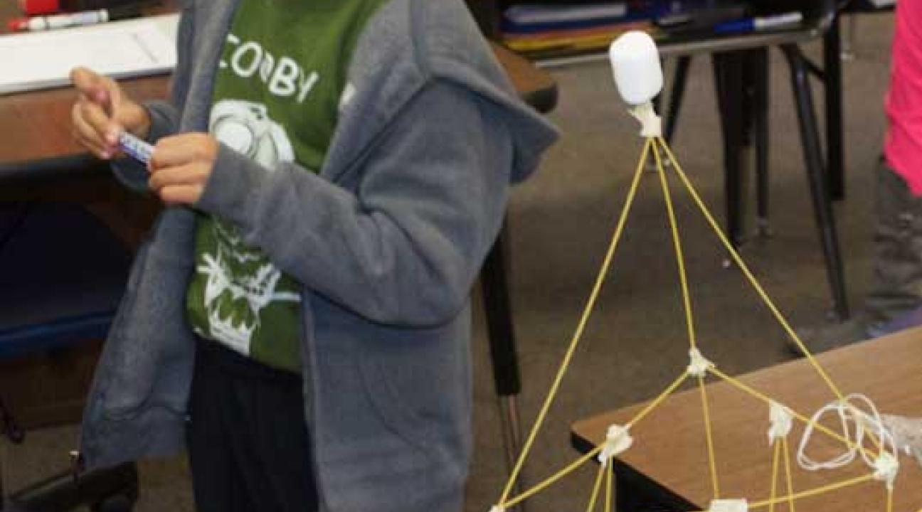 Boy looking to the right, a small structure is in font of him.