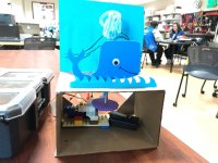 A paper Whale is on top of a box, with electronic and legos inside the box