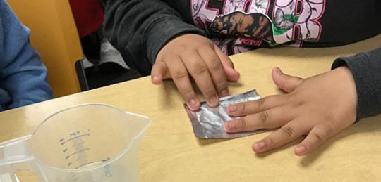 Student flattening a small piece of foil on a table.