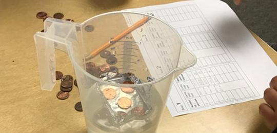 Coins and spreadsheet on a table next to a pitcher of water.