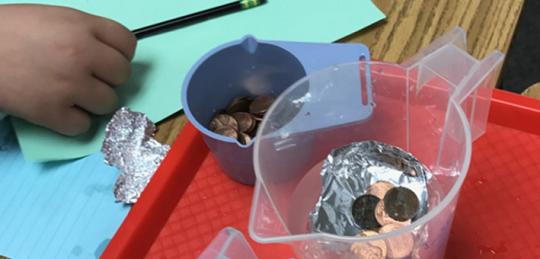 Cup of coins next to a pitcher of water with foil and coins floating inside.