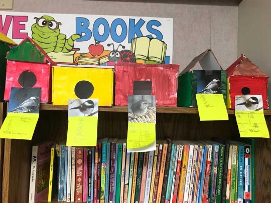 5 birdhouses on top of a bookshelf.  There are 3 red, 1 yellow and 1 green birdhouses.