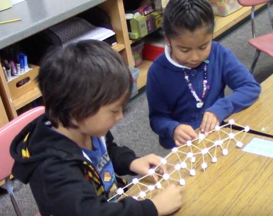 2 children woking on a bridge made of sticks.