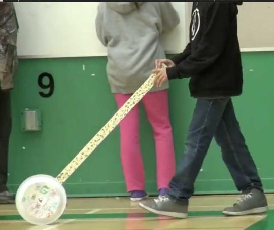 A white paper plate is attached to one end of a yardstick.