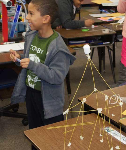 Boy looking to the right, a small structure is in font of him.
